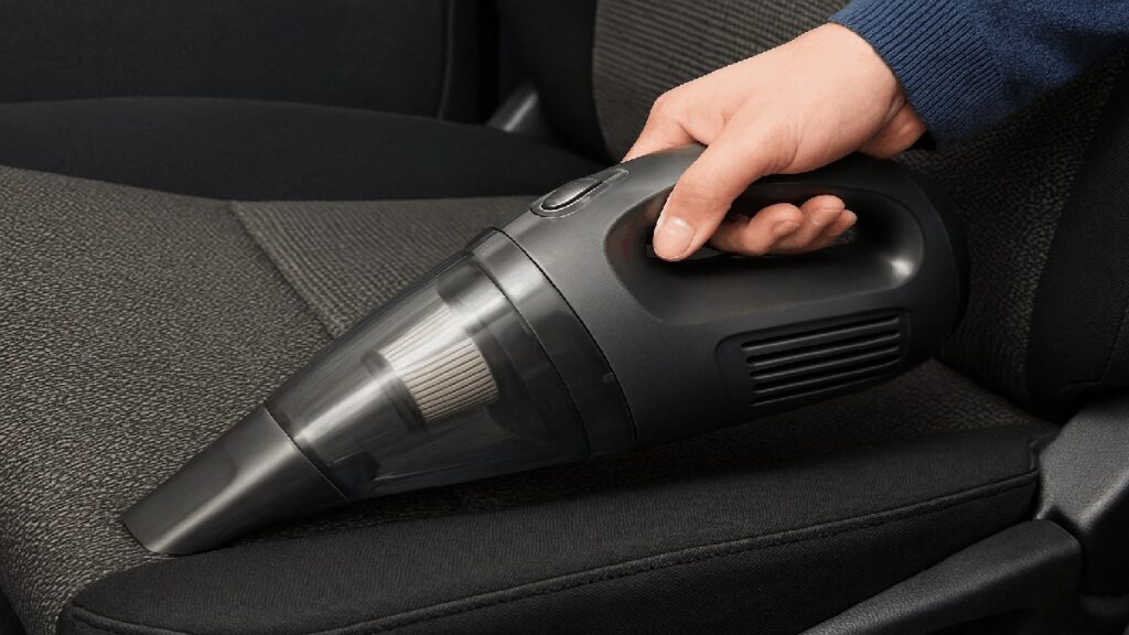 自動車のシートの隙間を、コードレス掃除機で掃除している手元の写真。掃除機を握っている様子